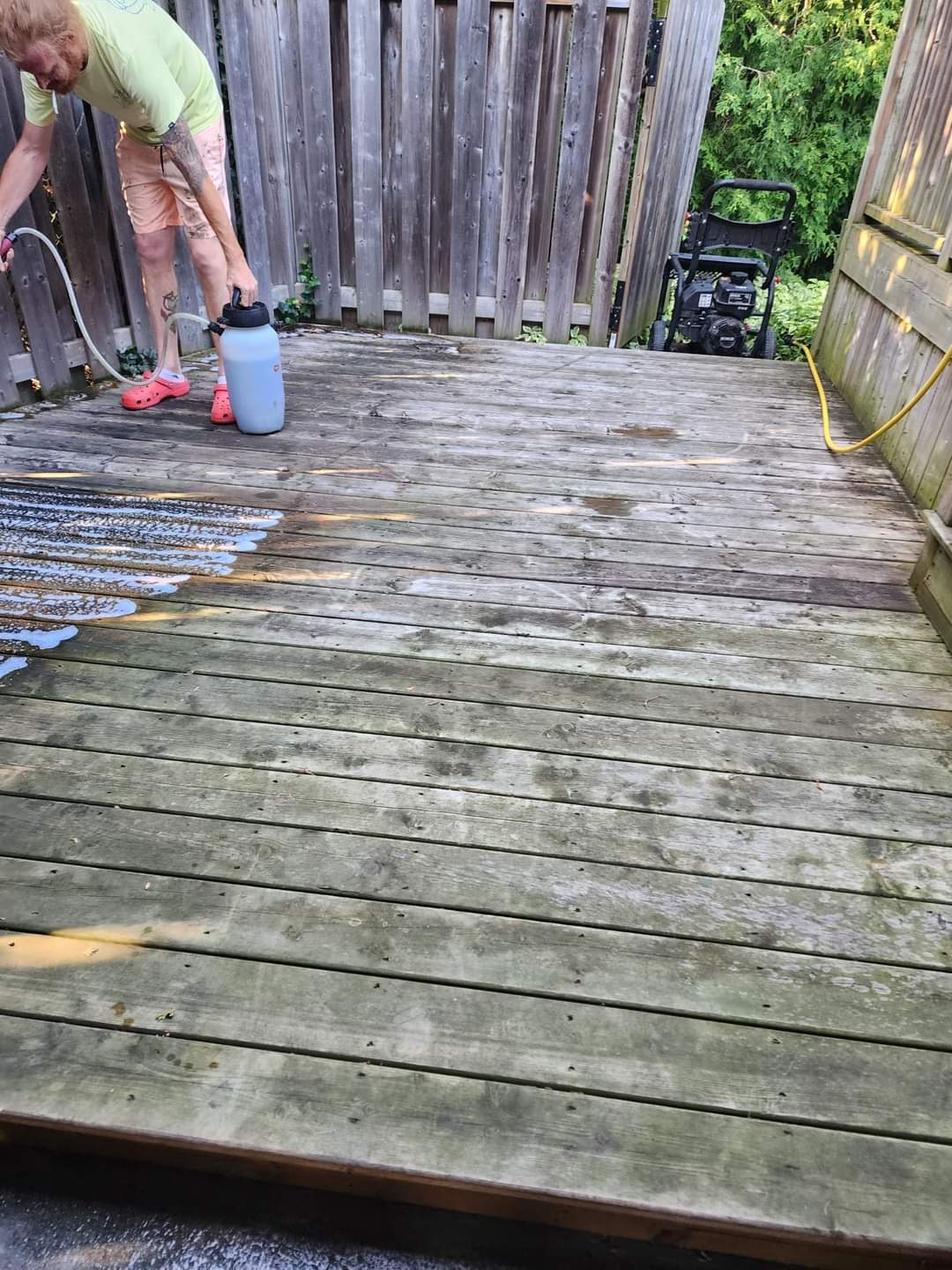 Crew member pressure washing a weathered grey deck